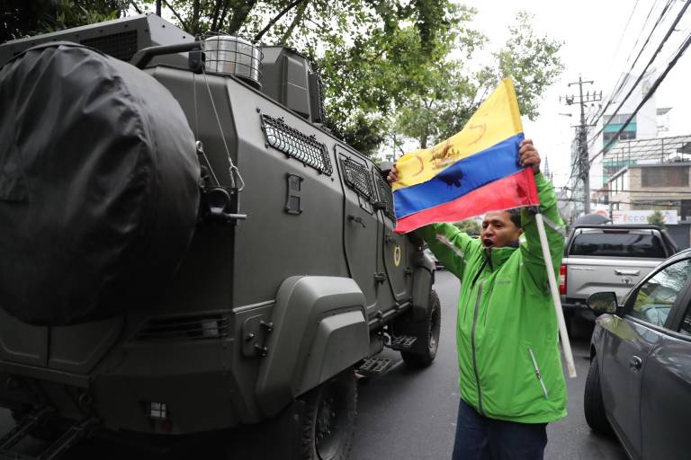 $!Un hombre exhibe una bandera mientras pasa un vehículo blindado donde es trasladado el exvicepresidente ecuatoriano Jorge Glas, el 6 de abril en Quito.
