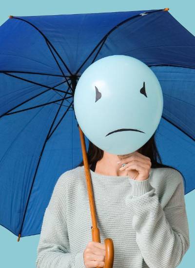 Mujer sosteniendo un paraguas azul y un globo con cara triste. Esta imagen representa el Blue Monday, el que se afirma es el día más triste del año.