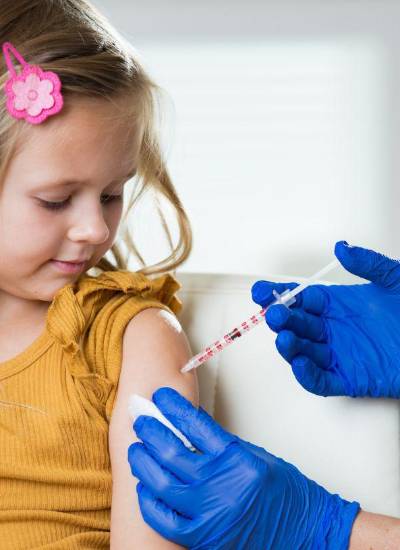 Niña recibiendo dosis de vacuna por una profesional de la salud.