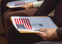 Personas sostienen carpetas del USCIS y banderas de EE.UU. durante una ceremonia de naturalización.