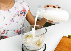 Una mujer vertiendo leche en un procesador.