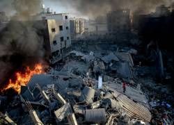 El humo y el fuego se elevan desde un edificio derribado mientras la gente se reúne en medio de la destrucción tras un ataque israelí en la ciudad de Gaza el 26 de octubre de 2023.
