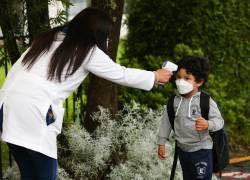 Una docente toma la temperatura a un estudiante en una escuela a las afueras de Quito.