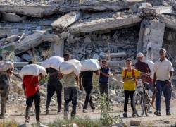 Personas caminan con bolsas de ayuda humanitaria recibidas en un centro de distribución gestionado por la Fundación Humanitaria de Gaza (FGH), respaldada por Estados Unidos e Israel, junto a los escombros de un edificio derrumbado.