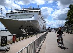 Un hombre pasa en bicicleta junto al crucero Ambition, registrado en las Bahamas, después de que los pasajeros fueran puestos en cuarentena.