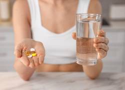 Mujer con un vaso de agua y pastillas en una mesa en el interior.