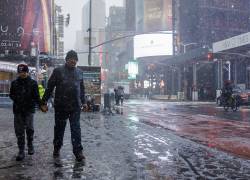 New York (United States), 13/02/2024.- La gente camina en la acera cerca de Times Square mientras la nieve cae en New York.