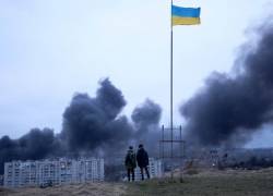 Dos personas que se encuentran cerca de una bandera nacional ucraniana observan cómo se eleva el humo oscuro luego de un ataque aéreo en la ciudad de Lviv, en el oeste de Ucrania, el 26 de marzo de 2022.