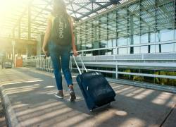 Mujer joven con equipaje de viaje en exteriores de un terminal.