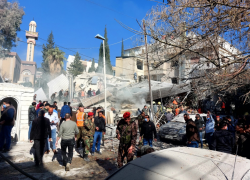 Varias personas y fuerzas de seguridad se reúnen frente a un edificio destruido por un ataque israelí en Damasco.