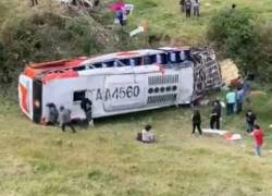 Fotografía que muestra el bus volcado y varios de los pasajeros de pie.