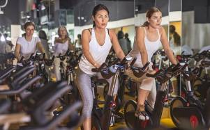 Cuatro mujeres deportistas calentando en bicicleta en una clase de spinning en el gimnasio.