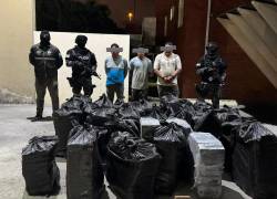 Fotografía que muestra cientos de bloques de cocaína colocados en bolsas. Detrás se aprecia a los tres detenidos por el caso.