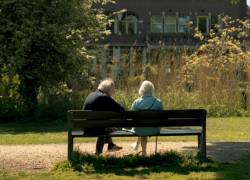 Dos adultos mayores sentados en la banca de un parque.