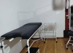 La imagen muestra un espacio de atención médica con una camilla vacía y otros implementos.