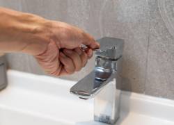 Hombre abriendo llave de agua en lavadero doméstico.