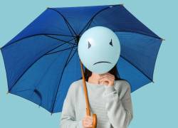 Mujer sosteniendo un paraguas azul y un globo con cara triste. Esta imagen representa el Blue Monday, el que se afirma es el día más triste del año.