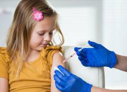 Niña recibiendo dosis de vacuna por una profesional de la salud.