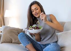 Mujer comiendo un bowl de ensalada en sofá.