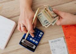 Mujer haciendo cuentas con dinero en la mano y usando una calculadora.