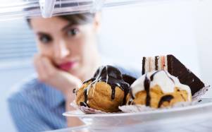 Mujer asomándose al refrigerador donde hay postres.