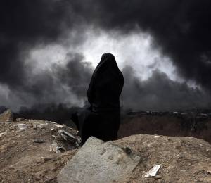 Una mujer iraní con velo, miembro de la Media Luna Roja de Irán, observa mientras el humo aún se eleva desde la refinería de petróleo de Shahran tras el ataque aéreo de anoche en Teherán.
