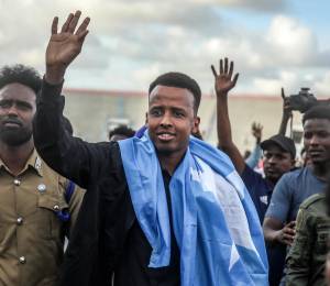 El árbitro Omar Abdulkadir Artan saluda a sus seguidores envuelto en la bandera somalí durante la bienvenida previa a un partido de fútbol solidario tras su regreso a Somalia en Mogadiscio.