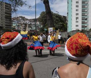 Unas mujeres llevan gorros navideños mientras observan a unos niños bailar en el barrio de El Valle (Caracas), el 1 de diciembre de 2021.