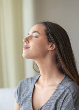 Mujer respirando aire fresco sentada en un sofá en casa.
