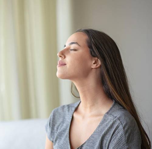 Mujer respirando aire fresco sentada en un sofá en casa.