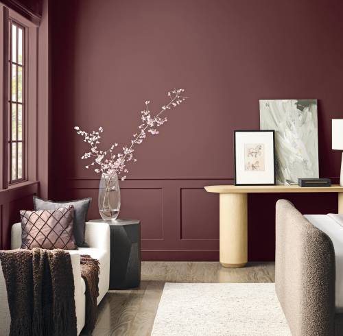 Habitación sofisticada con paredes en un profundo tono rojo marrón, molduras clásicas inferiores, un consola de madera clara de diseño minimalista y un sillón auxiliar con cojines decorativos.