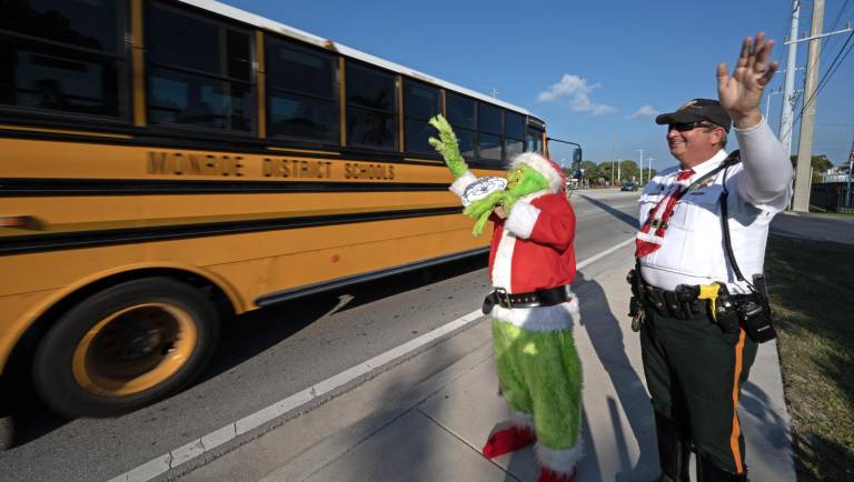 $!El coronel de la oficina del alguacil del condado de Monroe, Lou Caputo, disfrazado de Grinch, y el diputado Andrew Leird (d), mientras saludan a un autobús escolar que circula por la autopista Florida Keys Overseas.
