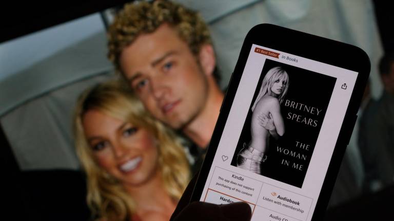 Esta imagen ilustrativa tomada el 21 de octubre de 2023 muestra la portada del libro de Britney Spears The Woman in Me de un minorista en línea frente a una fotografía de Britney Spears y Justin Timberlake en los American Music Awards del 9 de enero de 2002.