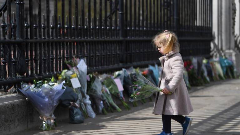 Una niña se dispone a colocar flores a la puertas del Palacio de Buckingham de Londres