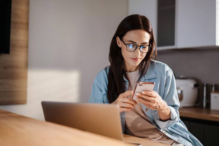 $!Mujer usando su teléfono inteligente mientras trabaja con su computadora.