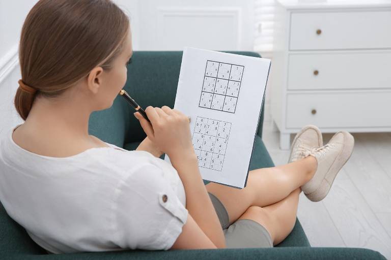 $!Mujer joven resolviendo un sudoku en el sofá de casa.
