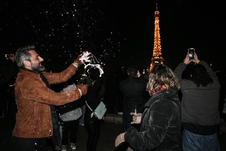 $!Un juerguista destapa una botella de champán cerca de la Torre Eiffel para dar la bienvenida al Año Nuevo, en el centro de París, el 31 de diciembre de 2025.