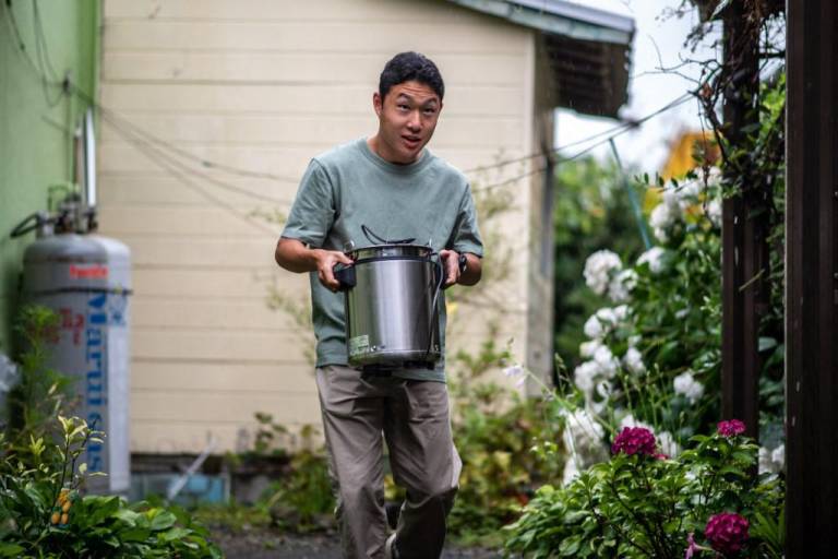 $!Koichi Miyatsu cargando una olla mientras se prepara para transportar platos de curry desde su casa a una iglesia como parte de un evento benéfico mensual para niños desfavorecidos en Kumamoto.