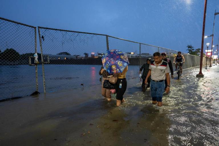 $!Personas caminan por una vía inundada debido a fuertes lluvias este martes, en Guayaquil.