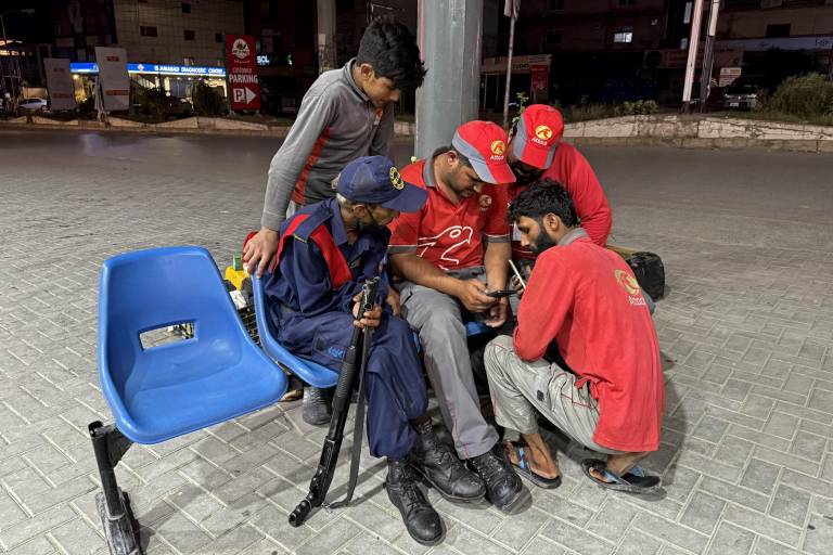 $!Los empleados ven las noticias en un teléfono móvil en una gasolinera de Islamabad.
