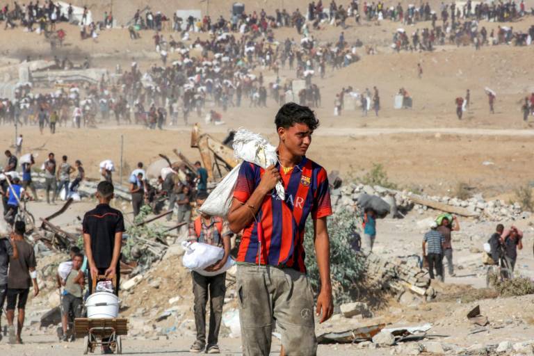 $!Personas caminan con bolsas de ayuda humanitaria recibidas en un centro de distribución gestionado por la Fundación Humanitaria de Gaza (FGH).