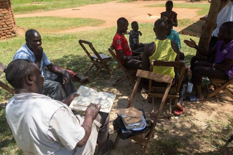 $!Musa Hasahya (izquierda) sostiene cuadernos que contienen detalles sobre su historia familiar, incluidos todos los nombres de sus 102 hijos y sus fechas de nacimiento, mientras está sentado frente a la casa de su familia en el distrito de Butaleja.
