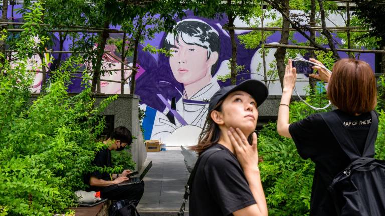 Una fan se toma una foto con el mural en progreso del grupo de K-pop BTS realizado en Seúl, que conmemora los 10 años de la banda.