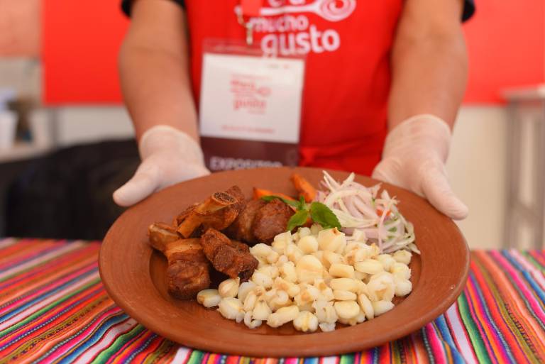 $!Stand de 'Perú Mucho Guato' de Tarwi Restaurante, presentando un plato Chicharrón de chancho al estilo caracino, un delicioso plato peruano que consiste en carne de cerdo frita lentamente, mote y sarza criolla.