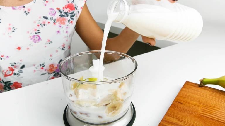 Una mujer vertiendo leche en un procesador.