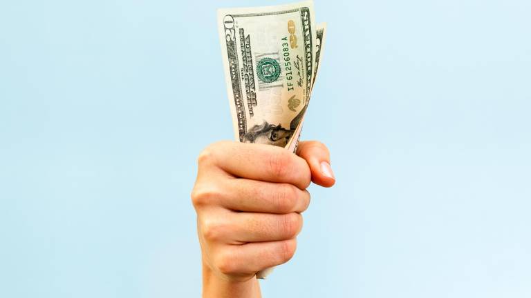 A hand holding a handful of twenty us dollars, on blue background.