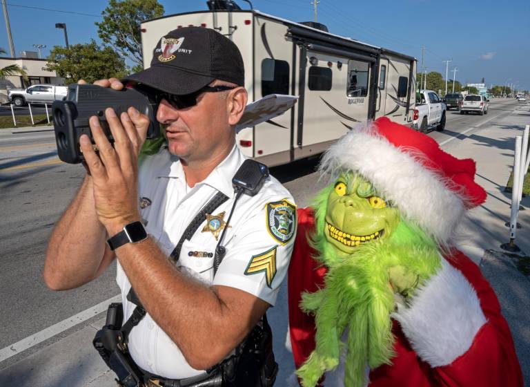 $!El coronel de la oficina del alguacil del condado de Monroe, Lou Caputo, disfrazado de Grinch, y el diputado Andrew Leird mientras miden la velocidad de conductores en la autopista Florida Keys Overseas.
