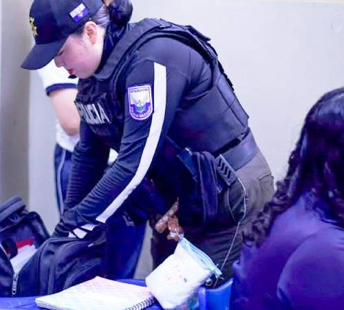 Fotografía de una agente revisando las pertenencias de estudiantes en un colegio de Guayaquil.