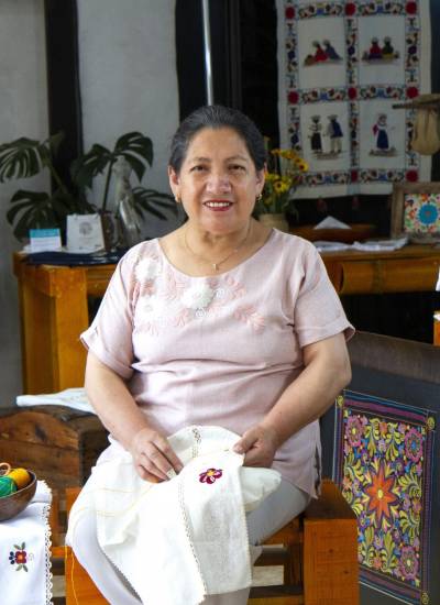 Teresa Casa Ponce, fundadora de Catelina, sentada junto a sus bordados dentro del taller donde capacita a quienes mantendrán la ancestral técnica.
