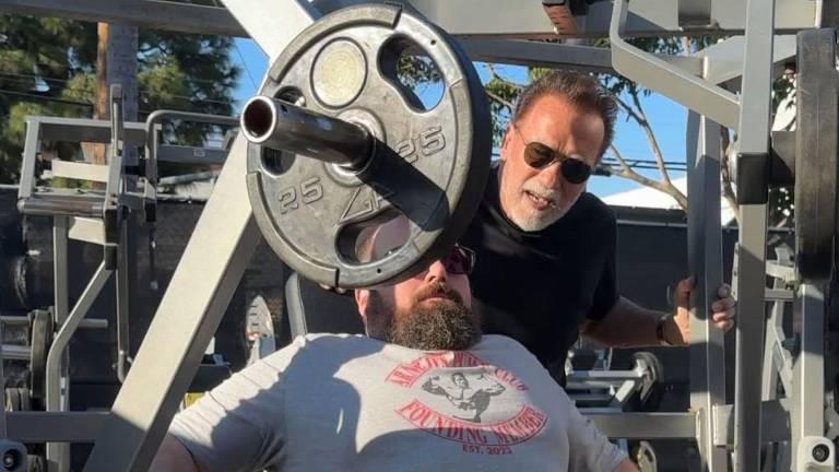 Imagen en la que se ve al fisicoculturista y actor, Arnold Schwarzenegger realizando trabajo de coach de entrenamiento físico.